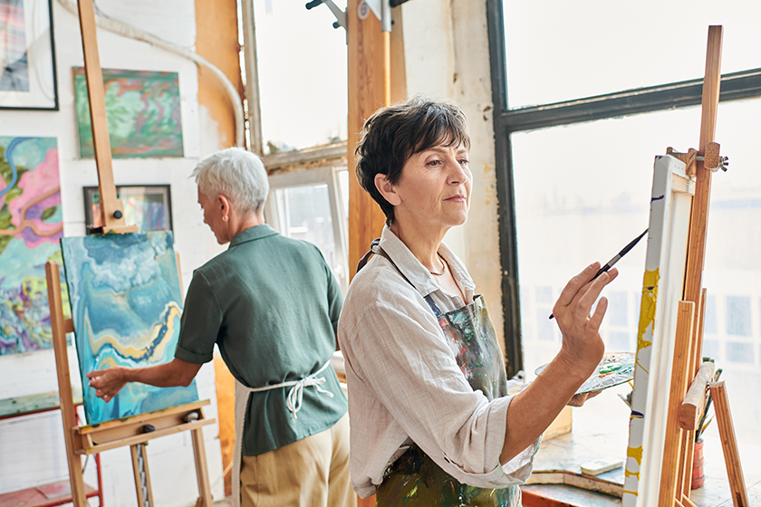 inspired-brunette-mature-woman-painting-easel-female-friend-art-workshop